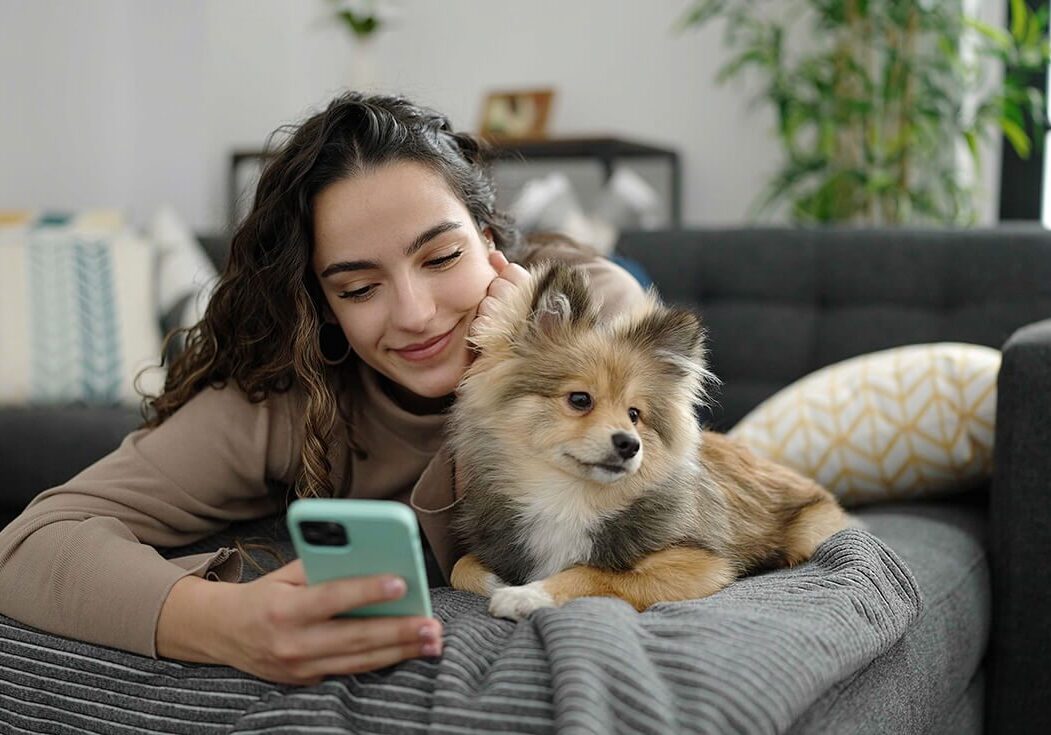 woman and small brown dog on sofa with phone